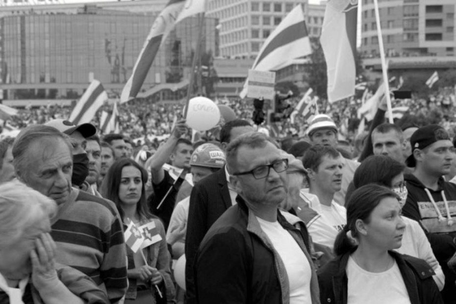 Czarno-biały kadr z filmu ,,Gdy kwiaty nie milczą". Na zdjęciu tłum smutnych, strajkujących ludzi z flagami.