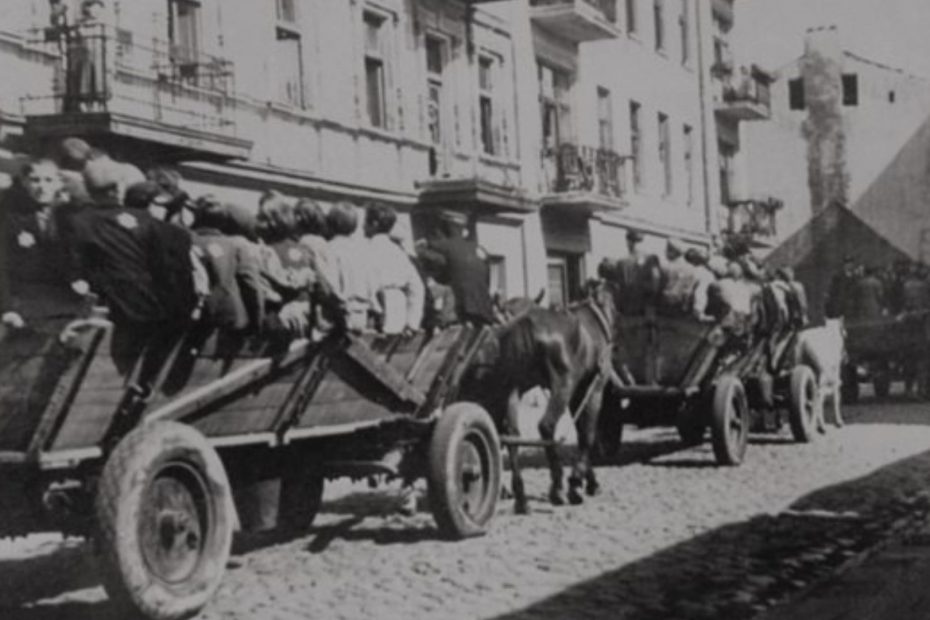 Czarno-białe zdjęcie na którym ukazane są wozy przeładowane ludźmi, ciągnięte przez konie.